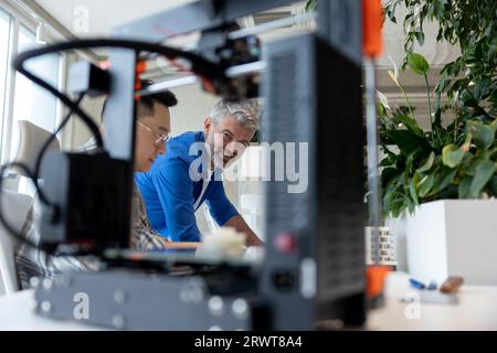 Two men architects using 3D printer in office and projecting house, drawing blueprints. Stock Photo