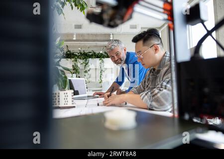Two men architects using 3D printer in office and projecting house, drawing blueprints. Stock Photo