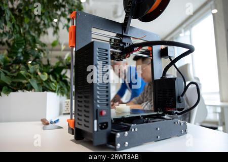 Two men architects using 3D printer in office and projecting house, drawing blueprints. Stock Photo