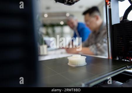 Two men architects using 3D printer in office and projecting house, drawing blueprints. Stock Photo