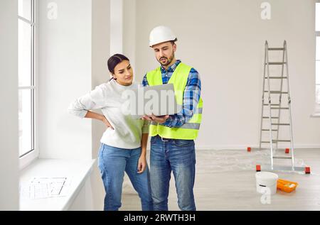 Builder or architect talking to young woman about interior decor and using laptop Stock Photo