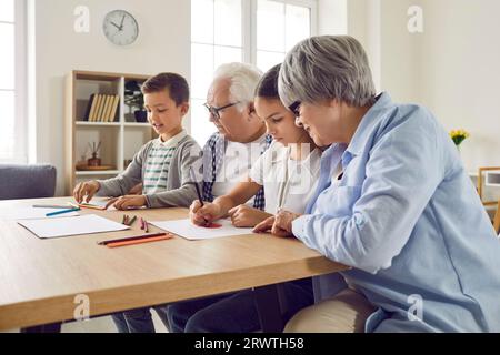 Senior couple grandparents spending time with grandchildren at home drawing at table. Stock Photo
