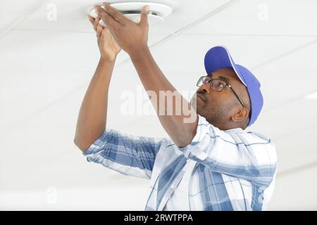 young electrician installing fire alarm unit on wall Stock Photo