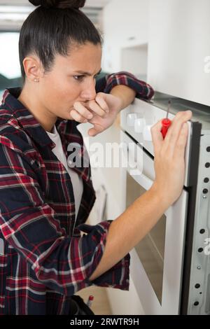 young woman looking oven using screw driver Stock Photo