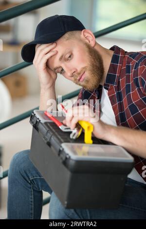 worried tradesman sat on stairs holding his toolbox Stock Photo