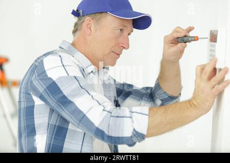 mature electrician installing security alarm on wall Stock Photo