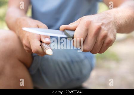 young man with a knife cut a wooden stick Stock Photo
