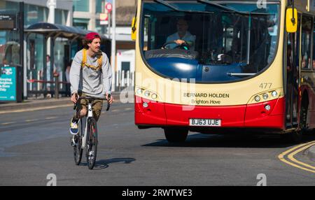 Young man riding a bicycle without helmet. Male cyclist cycling round a bus on a road in the UK, without wearing a cycle helmet. Stock Photo