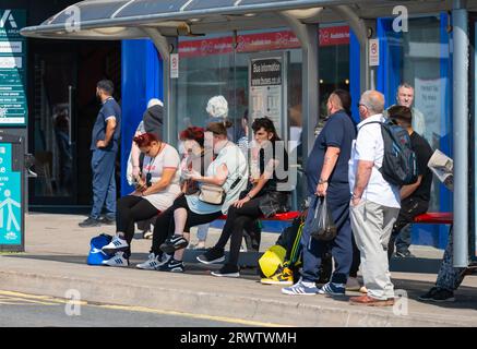 People, both men and women, sitting and standing waiting for a bus or busses at a bus stop in the UK. Stock Photo