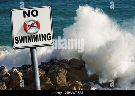 No swimming sign. Large waves of the sea break on the rocks on background. Stock Photo
