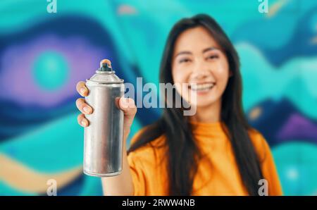 Smiling female street artist pointing spray paint can to camera. Urban street modern art concept Stock Photo