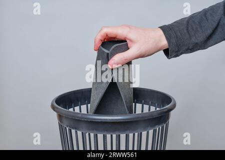 Person tosses a worn and well-used mouse pad into a trash bin. Stock Photo