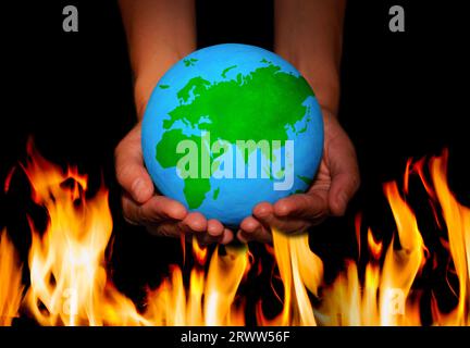 Pair of hands gently cradle a globe, hovering above a mesmerizing sea of flames. Delicate balance between the world and the fiery forces of nature. Stock Photo