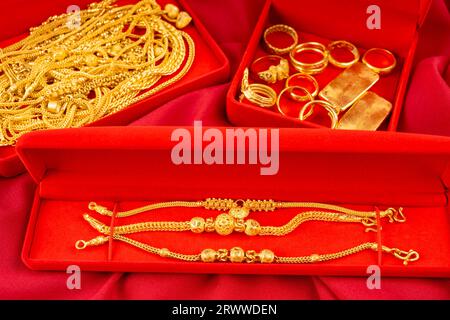 Many gold necklaces and gold bars in red box on red velvet cloth background. Stock Photo