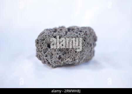 Unpolished black pumice rock cutout. Isolated over white fabric cloth Stock Photo