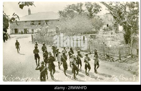 A marching band of boy scouts in uniform process down a quiet road past houses and gardens, playing their instruments. 2 copies Captioned in the negative: N…. boy [sprouts - sic]. Winnebah Gold Coast. Later manuscript caption: Native military band. Stock Photo