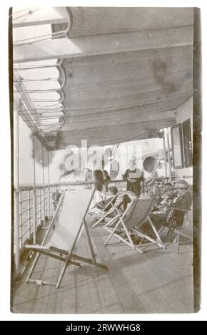 Alfred Tamlin stands amongst a group of fellow passengers on the canopied deck of a steamship. All are European, and some are seated in deckchairs. Later manuscript caption: Alfred Tamlin aboard ship right by funnel. Stock Photo