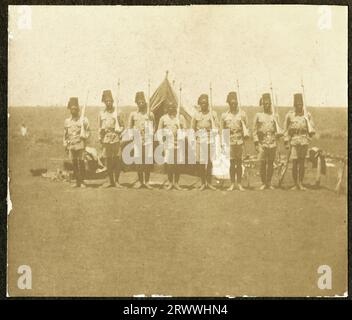 One of a series of four prints showing King's African Rifles soldiers leaving Nairobi to fight in German East Africa (Tanzania.) This print shows a column of European officers and African askari on parade in a wooded clearing, marching from left to right with a brass band playing on the right side of the picture.  Original page caption: Departure. 1/2nd Bn: K.A.R. August 4th 1916. Stock Photo