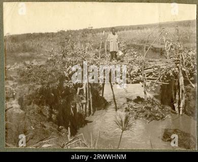 One of a series of four prints showing King's African Rifles soldiers leaving Nairobi to fight in German East Africa (Tanzania.) This print shows a railway carriage waiting at a station or siding prior to embarkation. In the background are piles of supplies and equipment, including a gun carriage, and a pitched tent. A number of European officers are talking in front of the carriage and African askari are standing around. Original page caption: Departure. 1/2nd Bn: K.A.R. August 4th 1916. Stock Photo