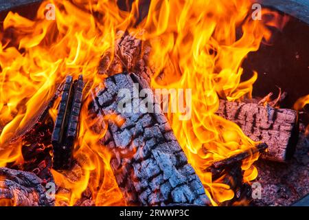 Close up of charred and burning logs inside intense fire with orange and yellow flames in fire pit Stock Photo