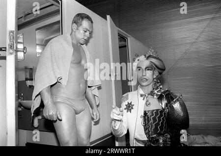 Andrew Logan 1980s UK. An artist and the organiser of the Alternative Miss World competition, a pansexual art, fashion beauty event. He is dressed as two halves of a whole, a man woman figure. Back stage before the start a muscle man comes out of the gent’s toilets. Grand Hall, Olympia, West London England 1981.   UK  HOMER SYKES Stock Photo