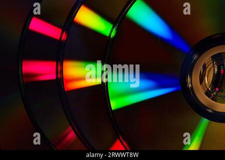 Abstract stack of four dark silvery CDs with reflective rainbow colored bursts of light on surface Stock Photo