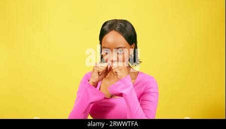 Serious strong Black woman punches arms, boxing fitness routine, yellow studio Stock Photo