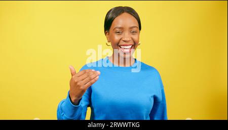 Friendly young woman beckons with hand 'come here', yellow studio background Stock Photo