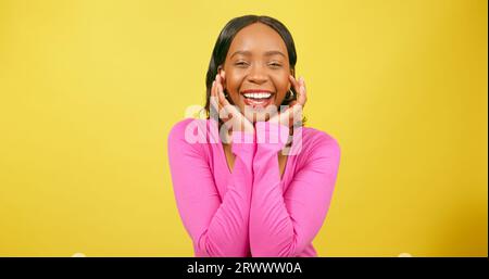 Beautiful Black woman cups hands under chin in cute pose, yellow studio Stock Photo