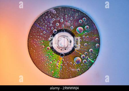 CD on gradient shift background with rainbow water drops on reflective metal surface Stock Photo
