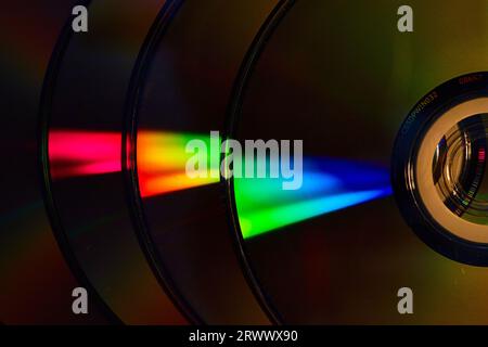 Abstract stack of four dark silvery CDs with reflective rainbow bursts of light on surface Stock Photo
