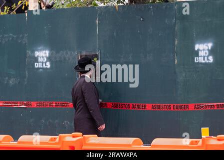 At a construction site in Brooklyn, an orthodox Jewish man can't resist looking at the ongoing construction through a hole. In Brooklyn, New York. Stock Photo
