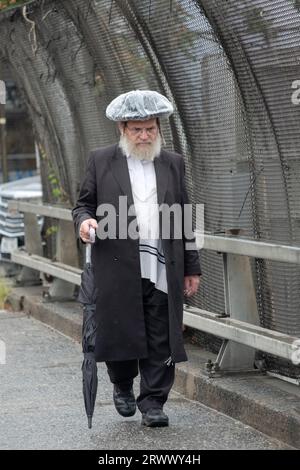 An older Jewish man walks during a light drizzle wearing a homemade rain hat. On Lee Avenue in Williamsburg, Brooklyn, New York. Stock Photo