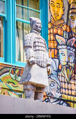 Chinese statue of man standing in front of soldier mural with bright blue windows Stock Photo