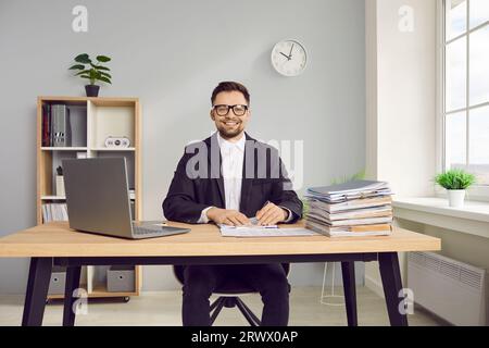 Young business man working at the desk on his workplace at office, looking at the camera smiling. Stock Photo