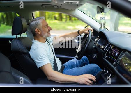 man in black suit holding hand on gear and smiling, driving car. Stock Photo