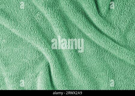 Terry cloth, green towel texture background. Wrinkled and crumped soft fluffy textile bath or beach towel material. Top view, close up. Stock Photo