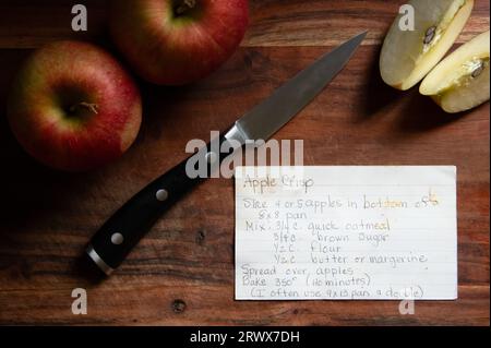 Handwritten apple crisp recipe card on wood cutting board with knife and apples Stock Photo