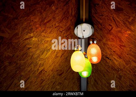 Hanging color lampshades on dark background. Composition of multi-colored chandeliers in interior design. Stock Photo