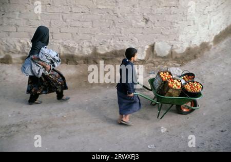 AL-MUKALLA, YEMEN-JULY 13, 2015; Boy together with his veiled mother on their way to the market with home grown vegetables Stock Photo