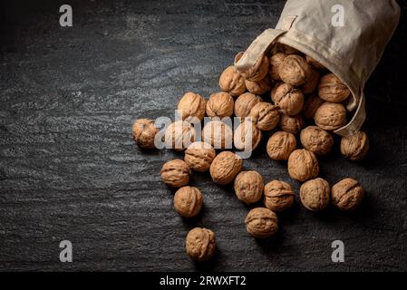 Walnuts in a bag scattered on dark background Stock Photo