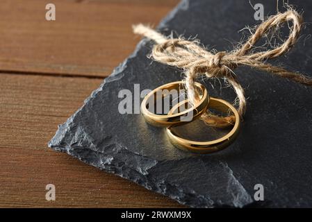 Detail of two gold rings joined with jute rope on slate stone on a rustic wooden table.. Top view. Stock Photo