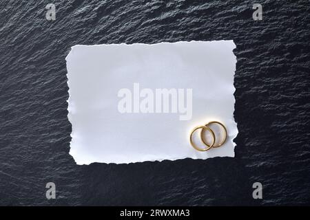 White textured paper card with two engagement rings on slate base table. Top view. Stock Photo