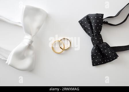 Gay wedding concept with black bow tie with polka dots and white on the sides of wedding rings in the center. Top view. Stock Photo