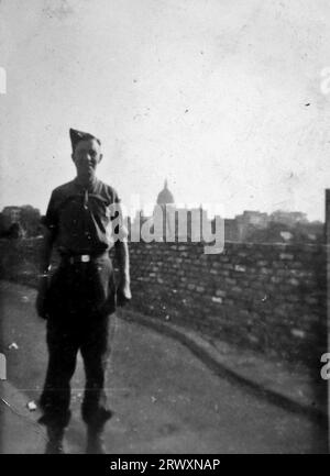 An isolated British soldier beside a brick wall, Chiswell Street, London, upon returning home. Rare photograph: From a collection compiled by an unknown British serviceman covering the No. 1 Composite Demonstration, AA Battery, tour of the USA, from July 11th 1943. This is one from over one hundred images in the collection which were on average around 4x3 inches. Stock Photo