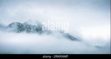 Moody, misty panoramic view of mountain peaks in clouds . Beautiful moody landscape with clouds, forest and mountains. Telemark, Norway. Stock Photo