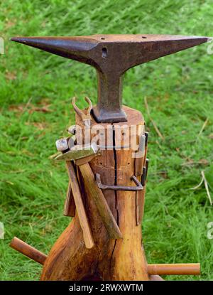 The metal anvil and other tools for blacksmithing on a background of green grass. Stock Photo