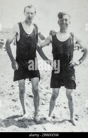 Archival photo of two young men standing on a beach wearing old-fashioned swimming costumes around 1920s Stock Photo