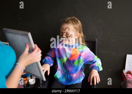 Young girl looking into a mirror and looking happy with her face painting of a leopard. Stock Photo