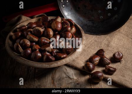 https://l450v.alamy.com/450v/2rwxyx9/chestnuts-on-a-wooden-plate-with-the-chestnut-roasting-pan-next-to-it-on-a-burlap-sack-2rwxyx9.jpg